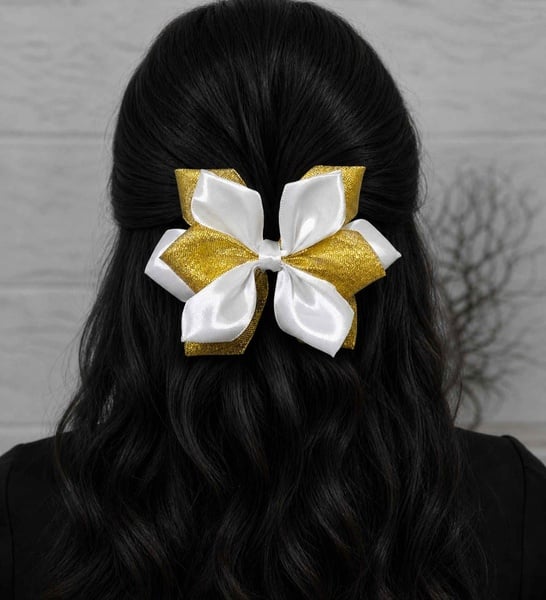 Rear view of woman with black hair in half-up style, secured with a gold and white satin bow, neutral background.