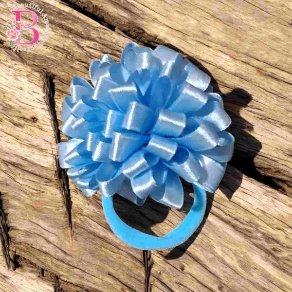 Pastel blue satin ribbon pom pom hair tie styled on natural wood, ideal for ponytails, school hair and cute everyday looks.