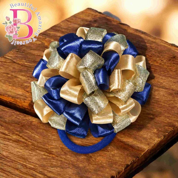 Navy blue and gold layered ribbon hair bow on elastic band displayed on rustic wooden surface with soft warm background lighting.