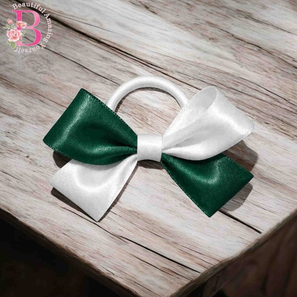 Green and white satin hair bow with white elastic band, displayed on rustic wooden background, elegant handmade ponytail accessory.
