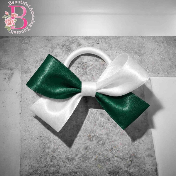 Green and white satin hair bow on a white elastic band, displayed on a textured grey background with elegant layered ribbon detail.