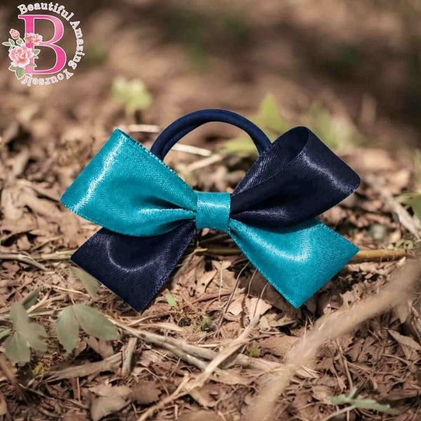 Turquoise and navy blue satin hair bow with elastic band, displayed outdoors on dry leaves with a glossy finish and elegant style.