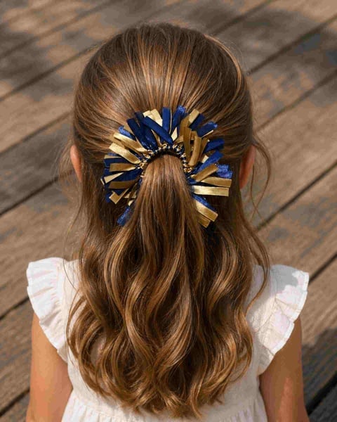 Girl viewed from behind wearing a navy and gold ribbon scrunchie bow in a ponytail on a driftwood deck outdoors.
