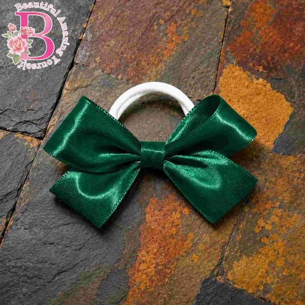 Emerald green satin hair bow with white elastic band on rustic autumn slate tile background, elegant handmade school hair accessory.