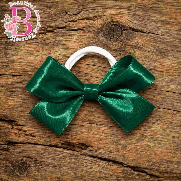 Emerald green satin school hair bow with white elastic band displayed on a rustic wooden background with Beautiful Amazing Yourself logo.