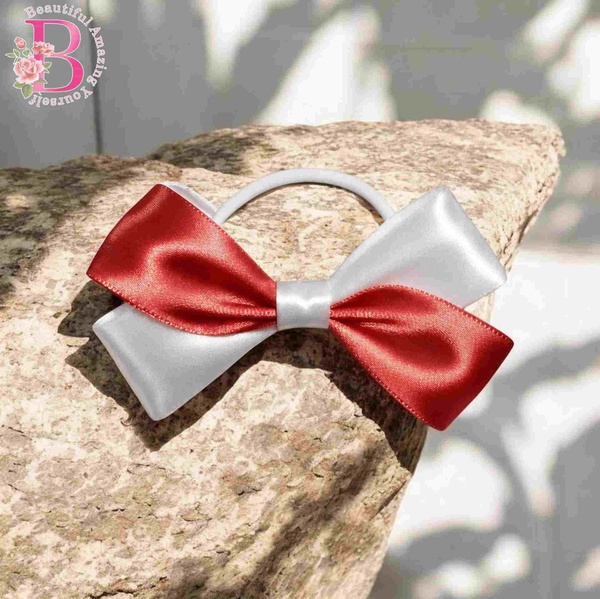 Red and white satin hair bow on a stone surface with a white elastic band, photographed outdoors in bright natural sunlight.