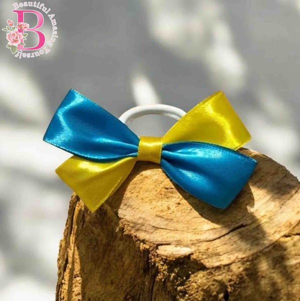 Turquoise and yellow satin hair bow on a white elastic band displayed on rustic driftwood with soft natural sunlight and shadows.