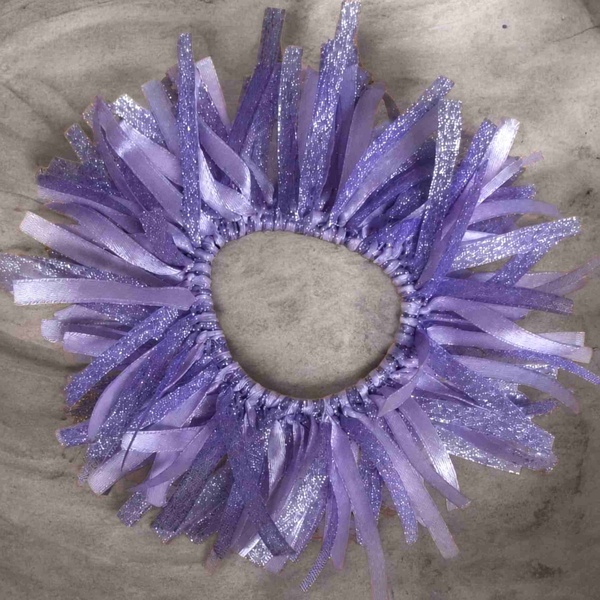 Lavender glitter ribbon scrunchie with layered satin and shimmer strands arranged in a circular design on a soft neutral background.