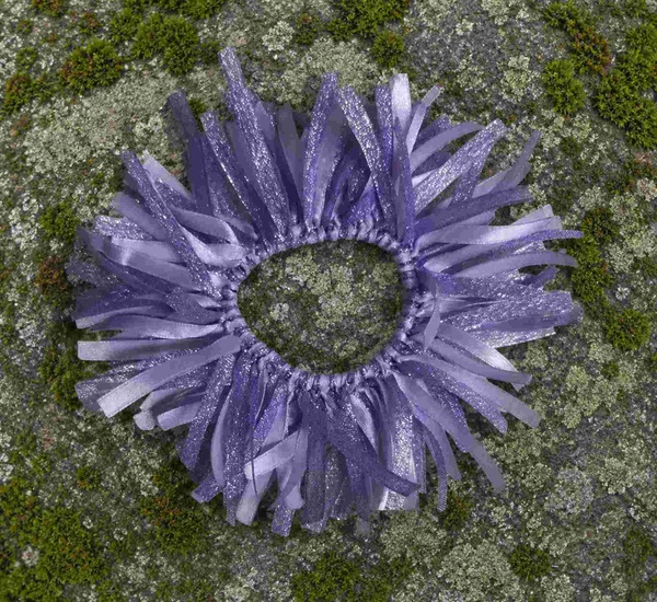 Lavender glitter ribbon scrunchie on a moss-covered rock surface, viewed from above with textured natural green background.