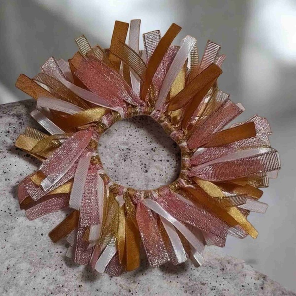 Pink, gold and peach ribbon scrunchie on a speckled stone surface with layered textured ribbons in soft neutral tones.