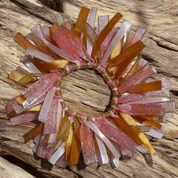 Pink, gold and peach ribbon scrunchie with layered satin and shimmer ribbons styled on rustic driftwood background.