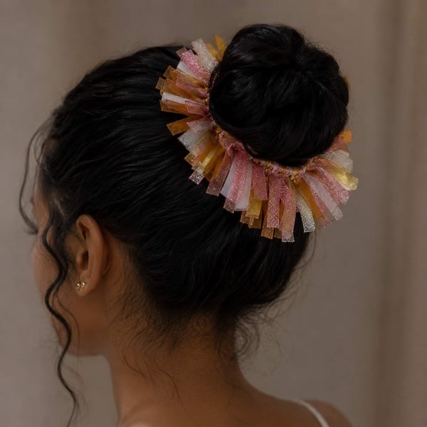 Pink gold and peach ribbon scrunchie styled around a black hair girl bun viewed from the left back with elegant shimmer ribbons.