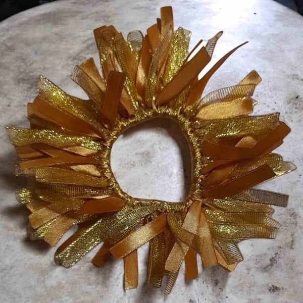 Gold ribbon scrunchie hair tie with layered metallic and satin strands arranged in a circular burst design.