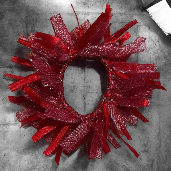 Sparkly red ribbon hair scrunchie with layered textured loops on a grey stone background, bold festive accessory style.