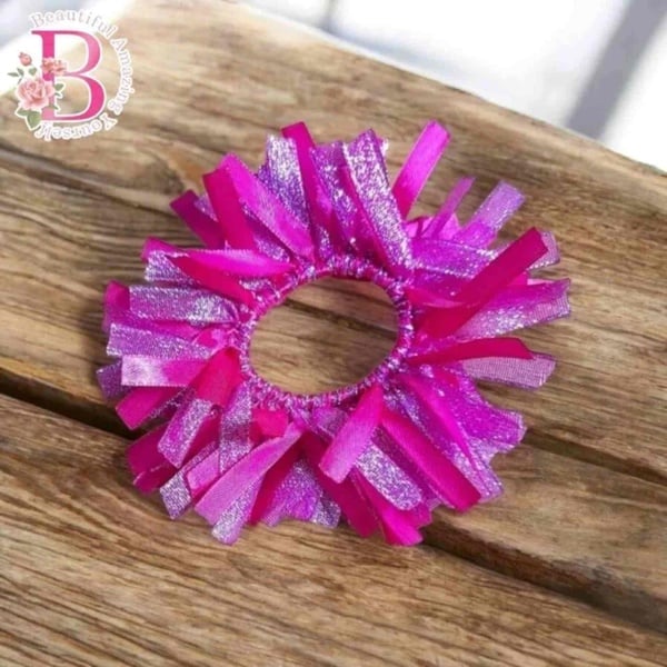 Bright pink and glitter ribbon scrunchie hair tie on a rustic wooden surface with soft lighting and playful textured strands.