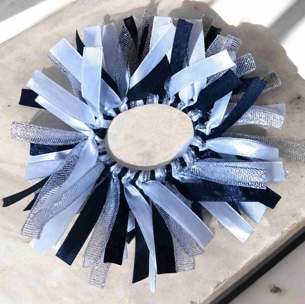 Black, white and silver ribbon scrunchie arranged in a circle on a light stone surface with soft sunlight and textured metallic ribbons.