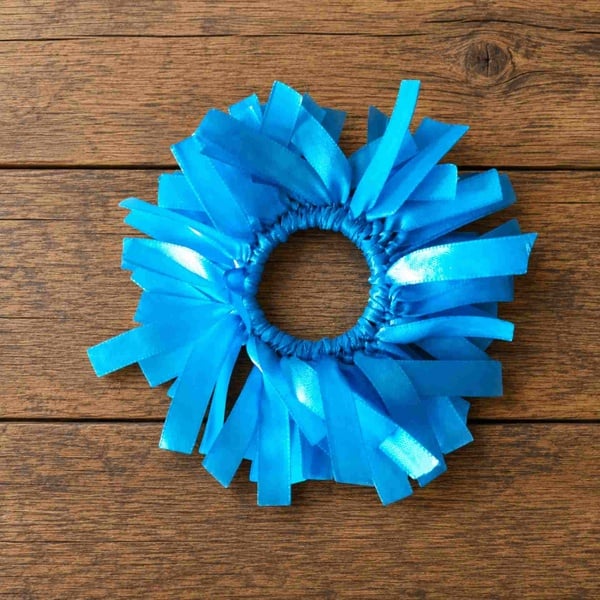 Light blue ribbon scrunchie on a rustic wooden tabletop, viewed from above with glossy ribbon strands arranged in a circular shape.