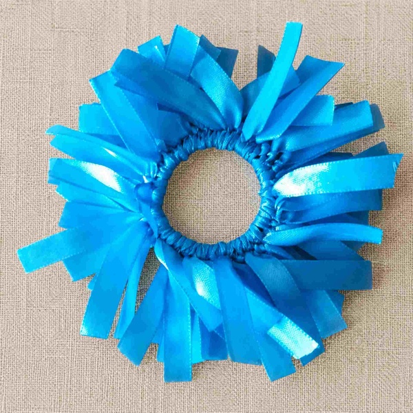 Light blue ribbon scrunchie with layered glossy strips arranged in a circular burst on a neutral linen fabric background.