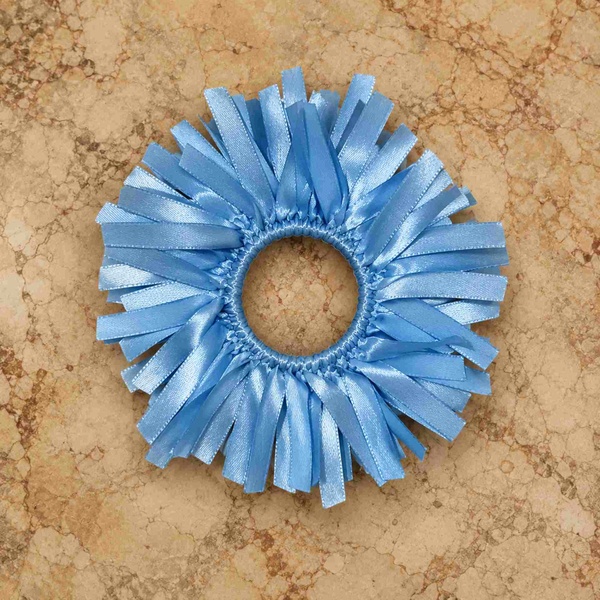 Light blue satin ribbon scrunchie photographed on an antique marble tabletop from above with detailed ribbon texture.