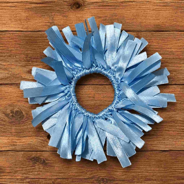 Handmade light blue ribbon scrunchie displayed on a rustic wooden tabletop viewed from above with soft natural lighting.