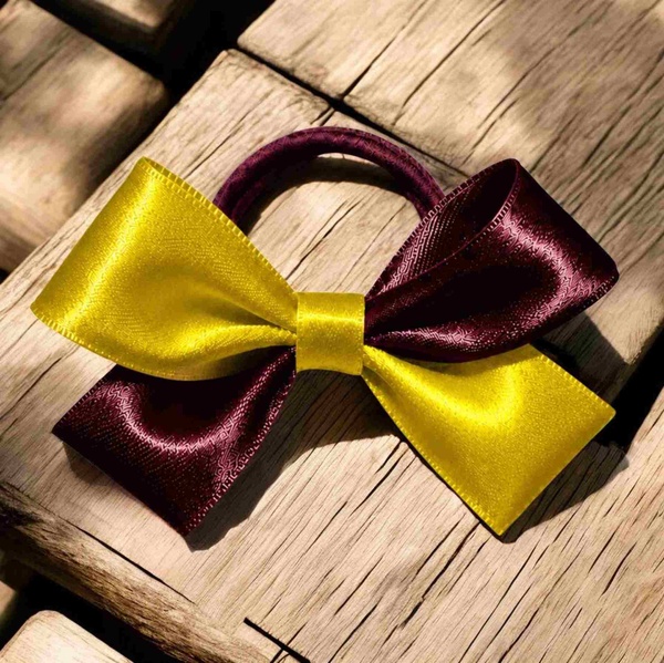 Maroon and yellow satin hair bow with a matching elastic band, displayed on a rustic wooden table with natural sunlight and shadows.