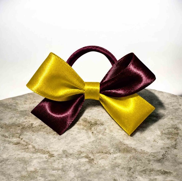Maroon and yellow satin cheer bow with a matching elastic band, displayed on a stone surface against a clean neutral background.