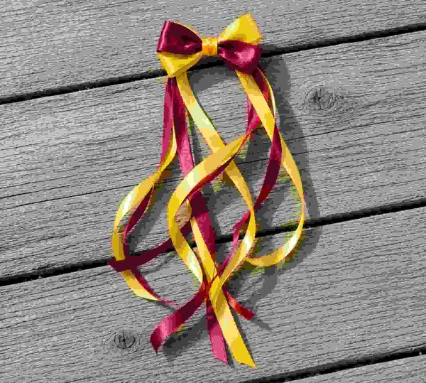 Maroon and yellow ribbon streamer bow with long curled tails on a grey wooden deck, featuring bright satin loops and flowing ribbons.