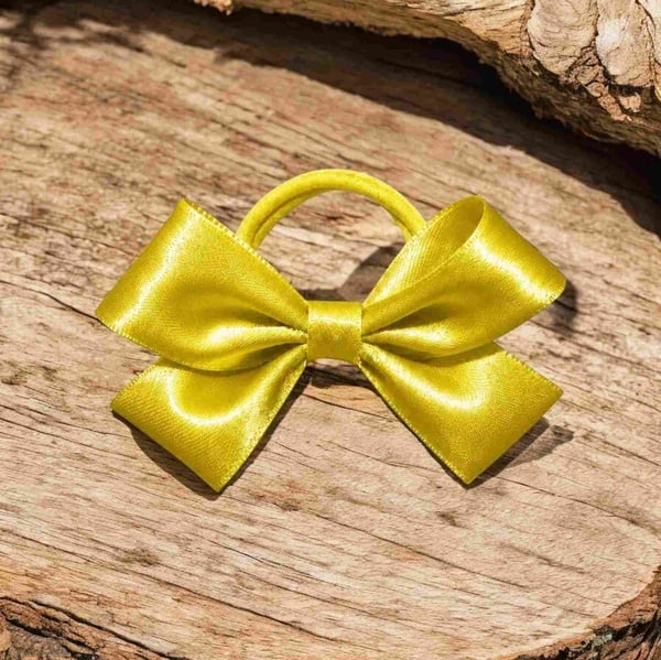 Shiny yellow satin hair bow with matching elastic band displayed on a rustic wooden surface, featuring smooth loops and a bright finish.
