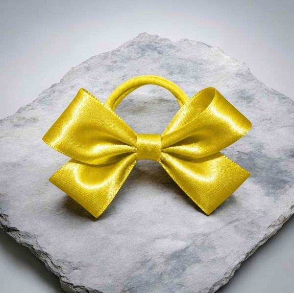 Bright yellow satin ribbon hair bow with matching elastic band, displayed on a textured gray stone slab background.