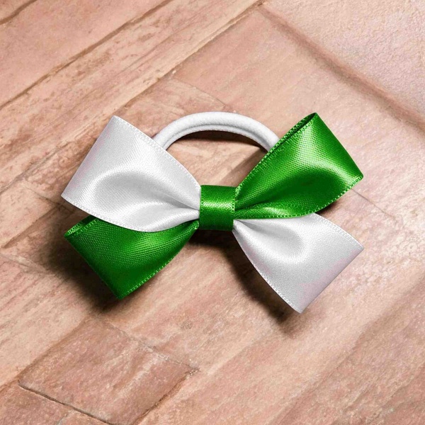 Green and white satin ribbon bow attached to a white elastic hair tie, displayed on a light wooden background with a glossy finish.