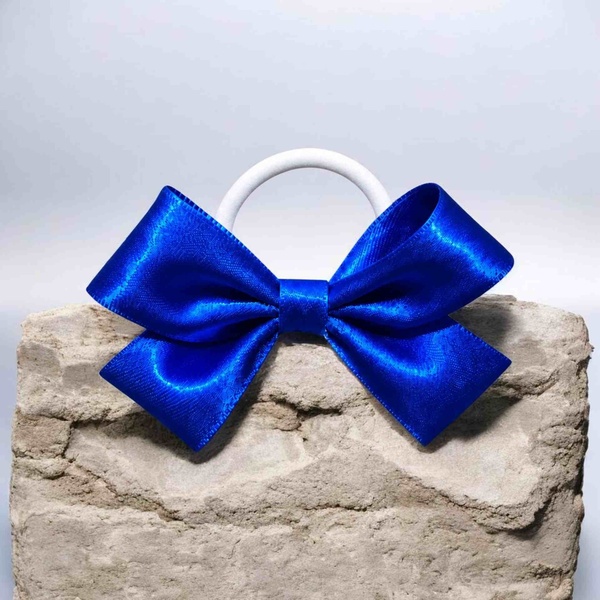 Royal blue satin hair bow with a white elastic band, displayed on a rustic stone block, featuring a glossy finish and classic style.