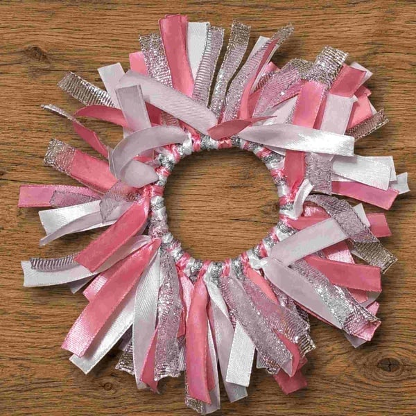 Pink, white and silver ribbon bun holder scrunchie on a rustic wooden surface, featuring layered satin and metallic ribbons.