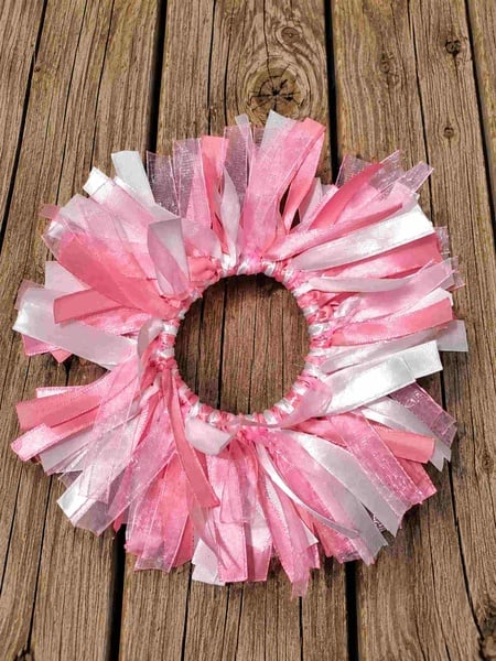 Pink and white ribbon bun holder scrunchie featuring layered satin and organza ribbons arranged in a fluffy circular design on rustic wood.