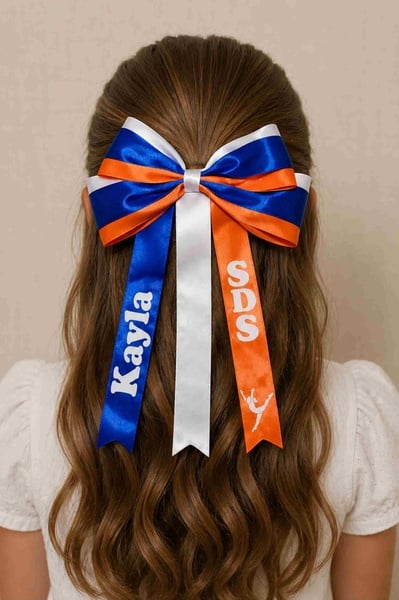 Girl viewed from behind wearing a personalised SDS dance hair bow in blue, orange and white satin ribbons with custom name print.
