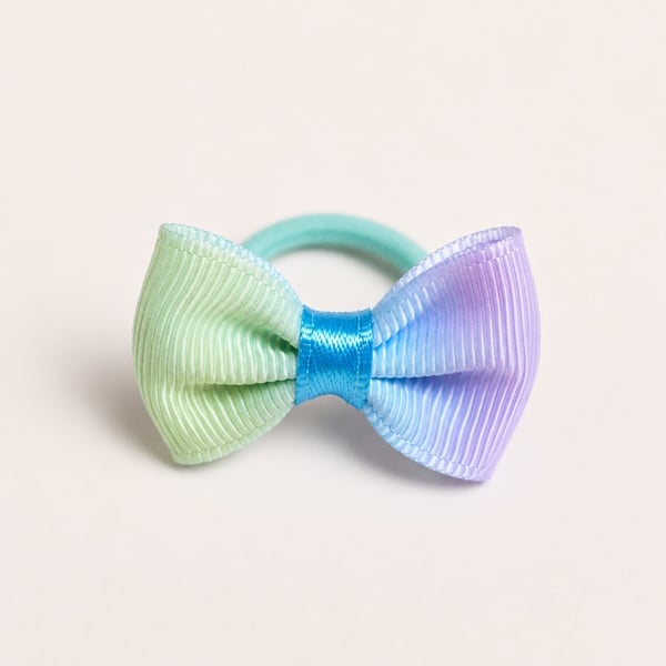 Pastel grosgrain ribbon hair bow on a mint elastic band, featuring soft green, blue and lavender tones on a neutral background.