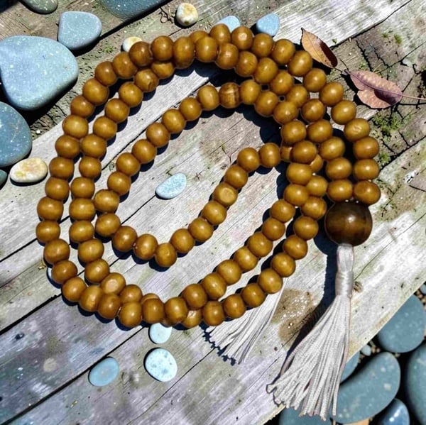 Natural wooden prayer beads with tassel arranged on weathered timber boards, surrounded by smooth stones and leaves outdoors.