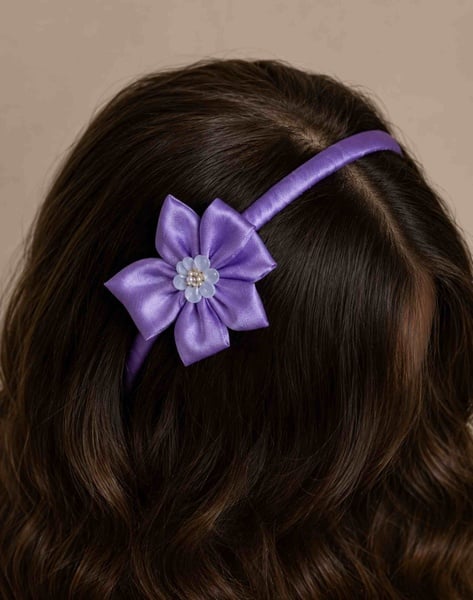 Purple floral satin headband displayed from a back top angle on glossy wavy brunette hair, highlighting the flower detail on a neutral background.