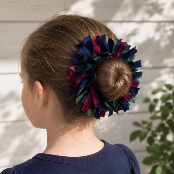 Rear left view of a girl's hair bun styled with a handmade navy, maroon and bottle green ribbon bow scrunchie accessory.