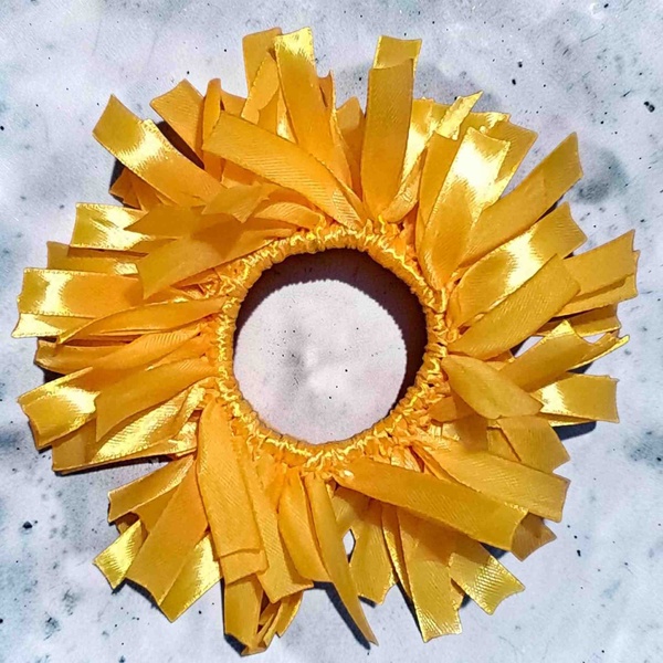 Sunflower yellow ribbon scrunchie with layered satin streamers arranged in a circular design, photographed on a light marble background.