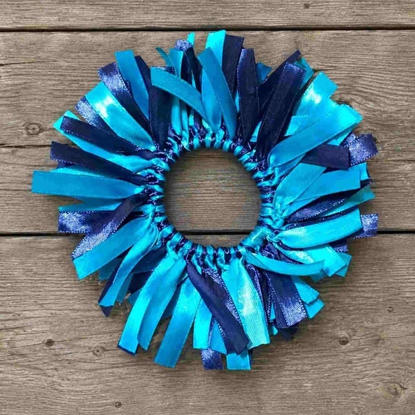 Handmade turquoise and navy ribbon hair bow displayed on a weathered driftwood deck surface in a top-view product photo.