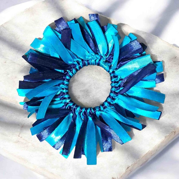 Turquoise and navy handmade ribbon bow displayed on a rough tile surface in a top-view product photography setting.