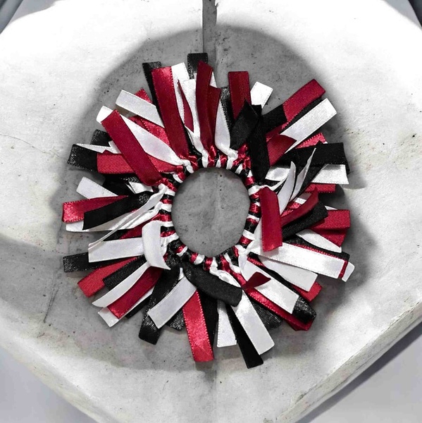 Handmade ribbon hair scrunchie with maroon, black and white satin streamers arranged in a full circular design on a stone dish.