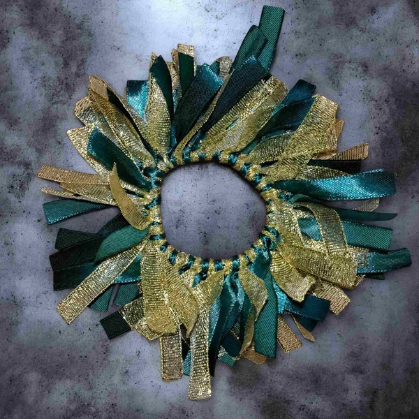 Green and gold ribbon scrunchie with shimmering metallic accents arranged on a textured gray backdrop, viewed from above.