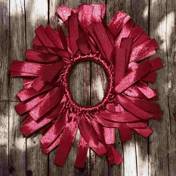 Handmade maroon ribbon hair scrunchie with layered loops and satin shine, displayed flat on a rustic wooden deck background.