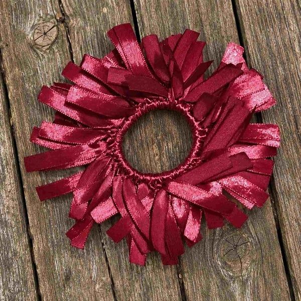Handmade maroon satin ribbon scrunchie with textured looped strands, displayed flat on a rustic weathered wooden deck surface.