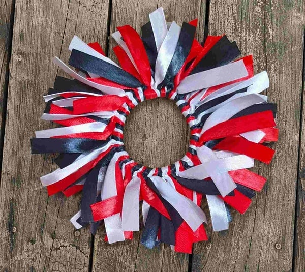 Red, white and black ribbon scrunchie hair tie displayed on a rustic weathered wooden deck, featuring layered ribbon strands.