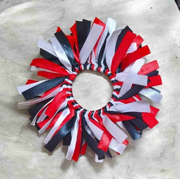 Red, white and black ribbon scrunchie hair tie arranged in a circle on a light stone surface, handmade for sporty hairstyles.