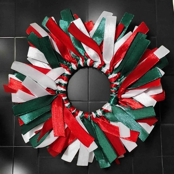 Red, white and green ribbon scrunchie with layered satin ribbon loops arranged in a full circular design on a dark background.