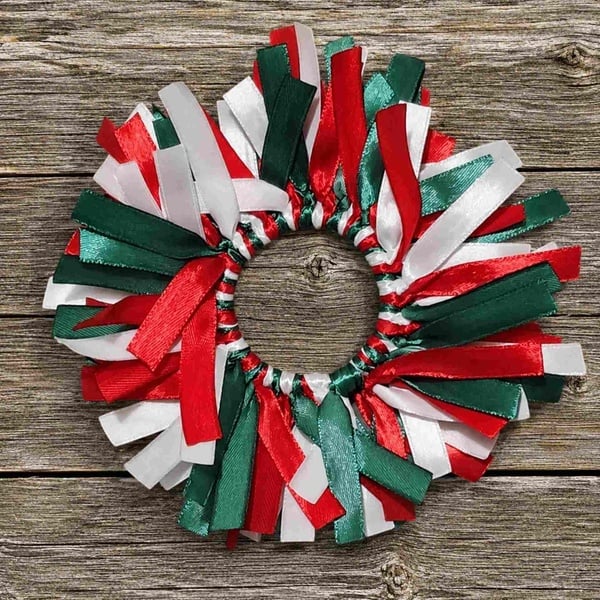Red, green and white ribbon hair scrunchie with layered satin streamers displayed on a rustic weathered wood deck background.