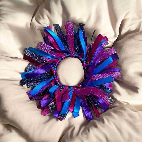 Pink, purple, blue, and black ribbon hair scrunchie with layered satin and glitter strands arranged in a fluffy circular design.